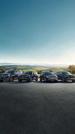 Lineup of Lincoln vehicles on road in front of hills
