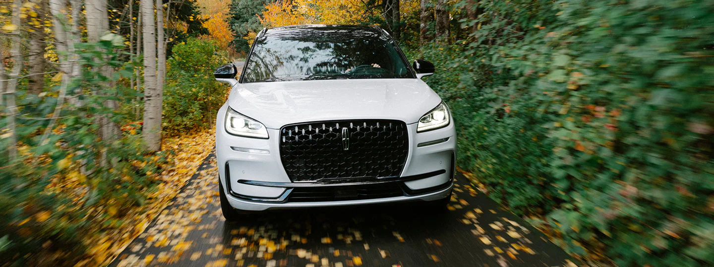 White Lincoln Corsair® Reserve SUV on a road with fallen leaves