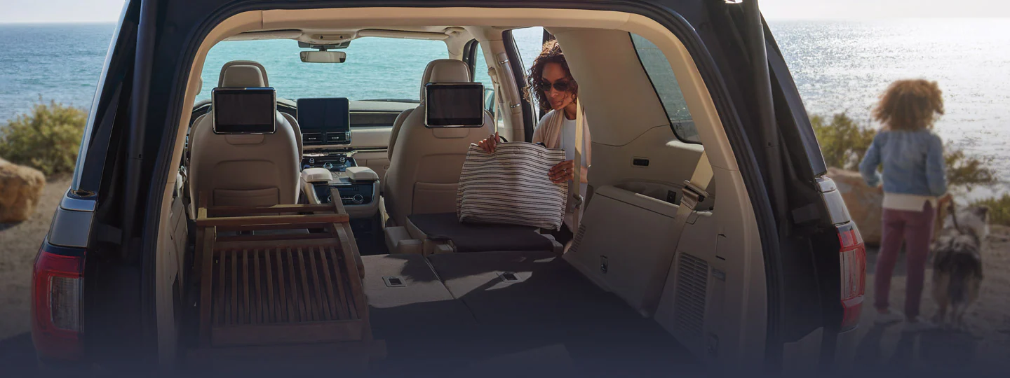 Woman loading Lincoln Navigator® SUV trunk by ocean with child and dog