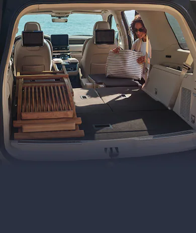 Woman loading Lincoln Navigator® SUV trunk by ocean with child and dog