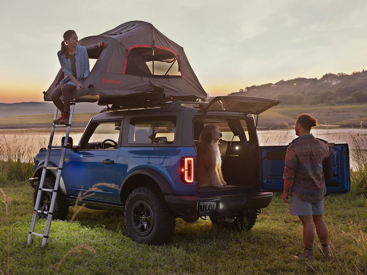 A 2025 Ford Bronco® with a rooftop tent and people camping next to lake