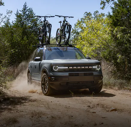A 2024 Bronco Sport® SUV driving down a dirt road with bikes loaded on a rack