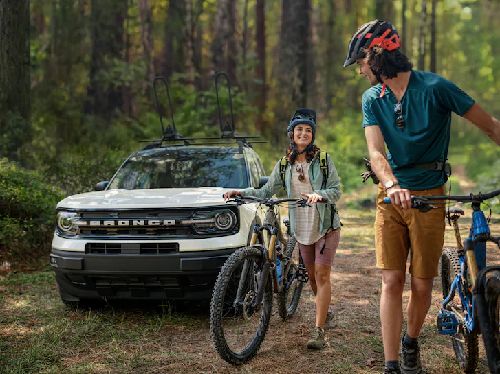A 2024 Bronco Sport® SUV in Oxbow White parked in forest as couple starts bicycling adventure