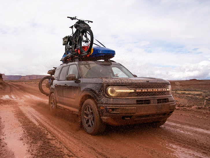 A very dirty 2024 Bronco Sport® SUV with bicycles and Thule roof storage being driven down dirt road