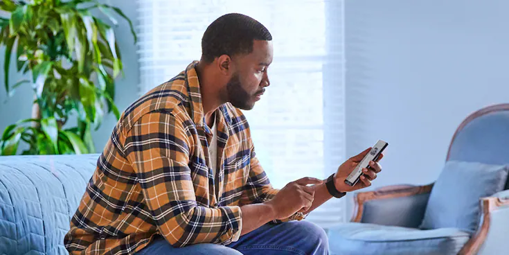 A man sitting on a plush living room couch using his smartphone