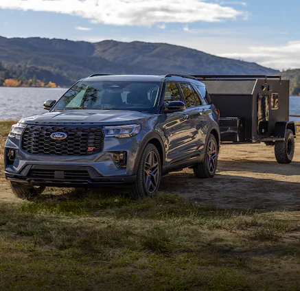 A 2025 Ford Explorer® SUV parked near a lake towing a trailer and near people going kayaking