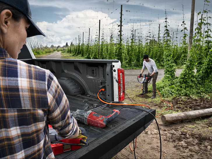 A man uses a posthole digger that is plugged into the bed of a Ford F-350 Super Duty® XLT