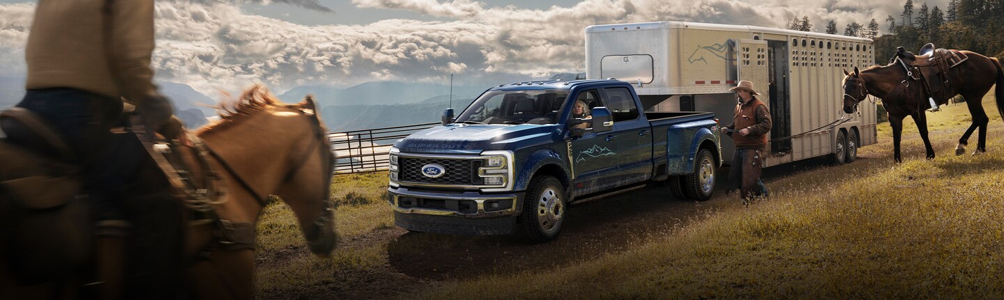 A Ford Super Duty®450® truck hauling a large horse trailer as cowboys load horses
