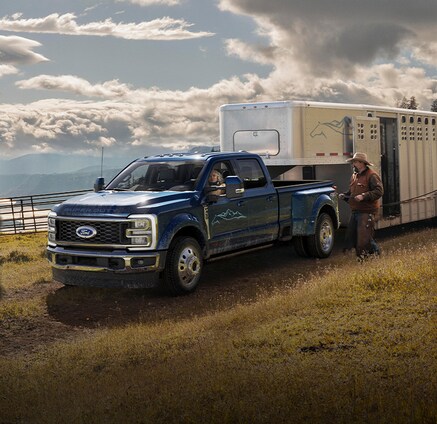 A Ford Super Duty®450® truck hauling a large horse trailer as cowboys load horses