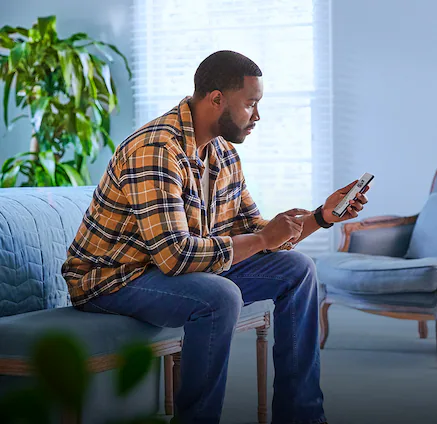 A man sitting on a plush living room bench using his smartphone