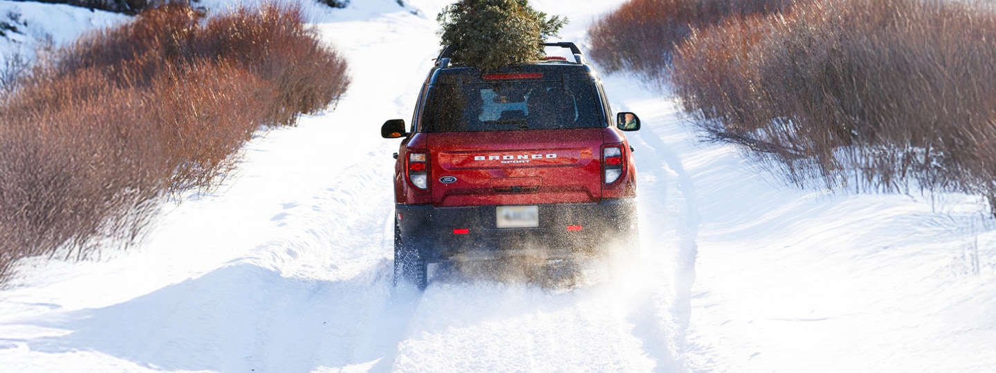 Red Ford Bronco® SUV driving through snowy landscape with a tree on top