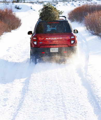 Red Ford Bronco® SUV driving through snowy landscape with a tree on top