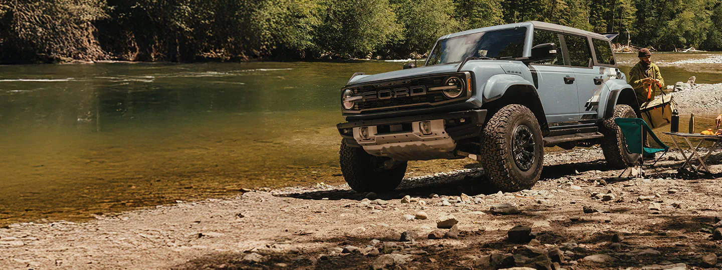A couple are camped on a river shore next to their Ford Bronco®