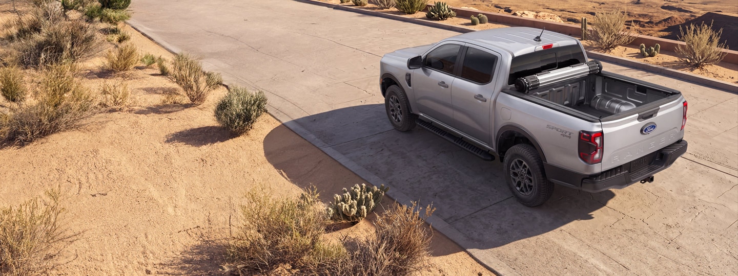 Silver Ford Ranger® truck parked on a desert road with a rolled-up cover in the truck bed