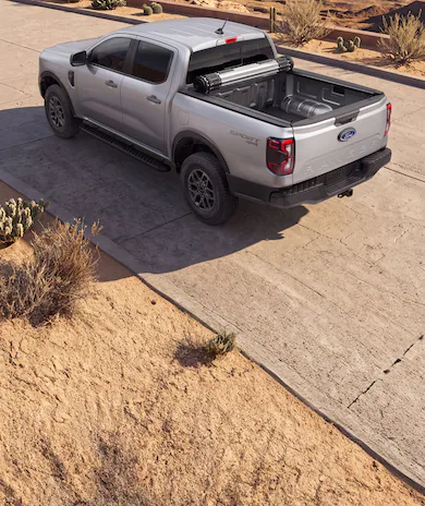 Silver Ford Ranger® truck parked on a desert road with a rolled-up cover in the truck bed