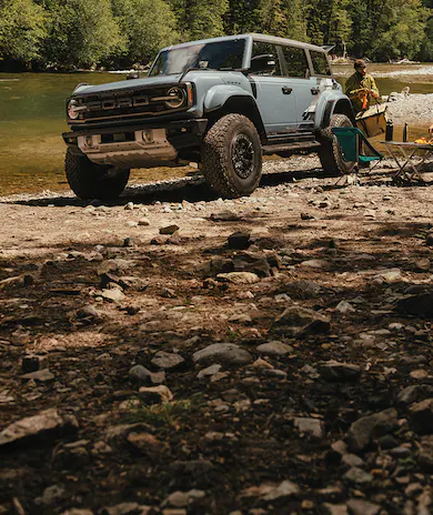 A couple are camped on a river shore next to their Ford Bronco®