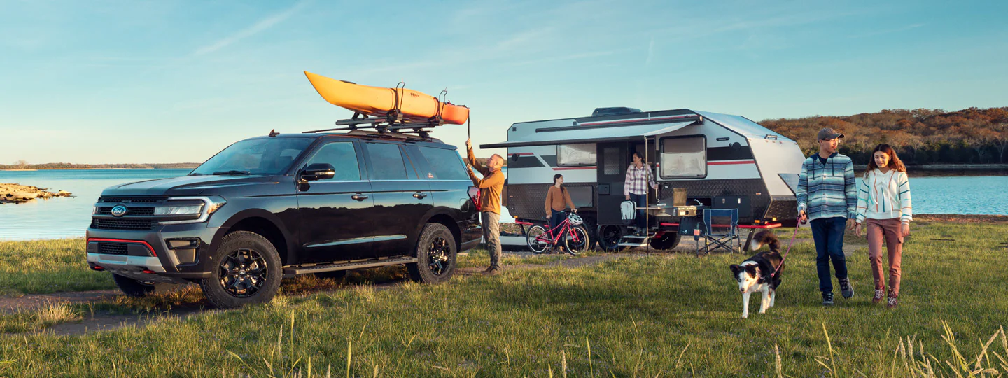 Ford Expedition® SUV with kayak, camper, family, and dog by lake