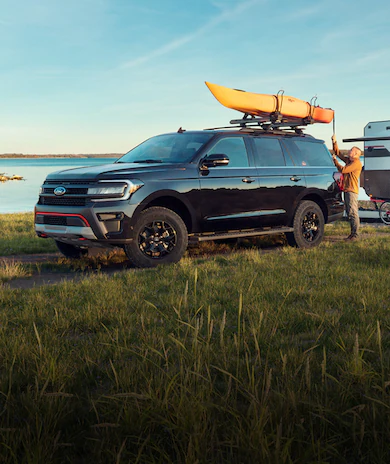 Ford Expedition® SUV with kayak, camper, family, and dog by lake