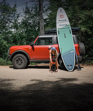 Woman and dog by orange Ford Bronco® SUV and paddleboard