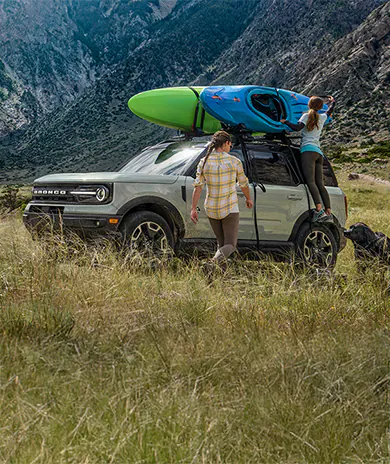 A 2025 Bronco® next to river with people handling kayaks on roof rack