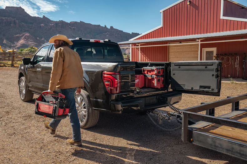 A cowboy walking past the open back end of a 2025 Ford F-150® pickup filled with tools