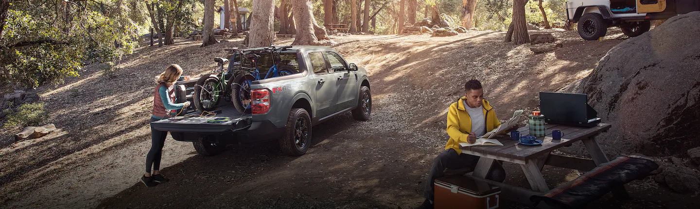 A 2024 Maverick® pickup with mountain bikes in bed with people camping