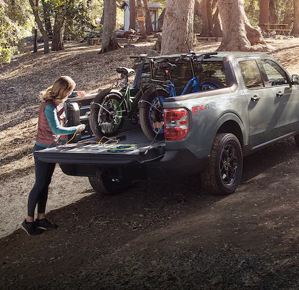 A 2024 Maverick® pickup with mountain bikes in bed with people camping