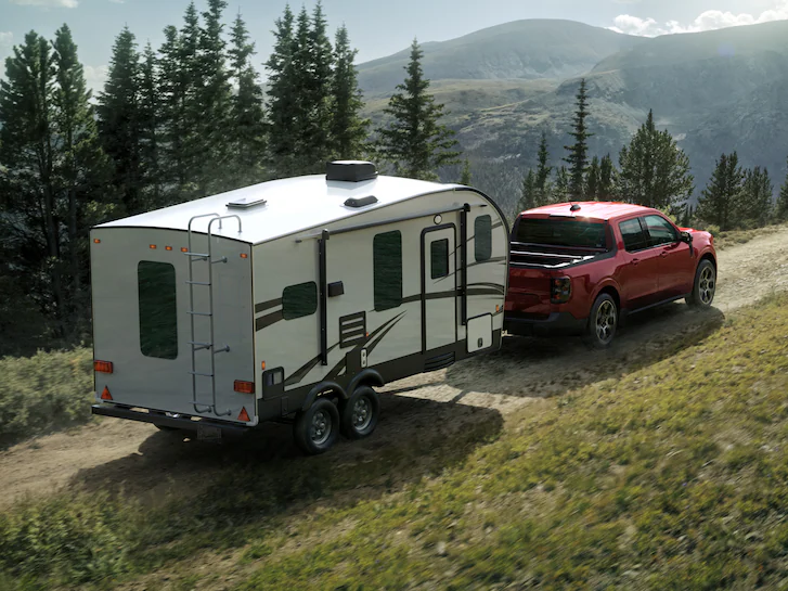 A 2025 Ford Maverick® LARIAT® pickup pulling a camper along a mountain dirt road