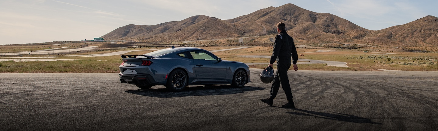 A driver walking toward a 2025 Ford Mustang® on a race course