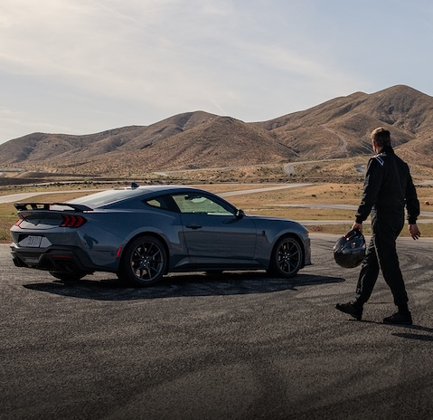 A driver walking toward a 2025 Ford Mustang® on a race course