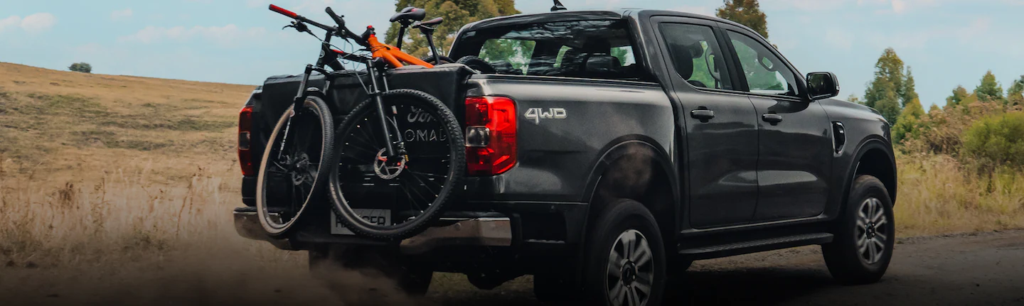 A 2025 Ford Ranger® being driven up a a dirt road with mountain bikes in bed and on bike rack