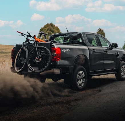 A 2025 Ford Ranger® bing driven up a a dirt road with mountain bikes in bed and on bike rack