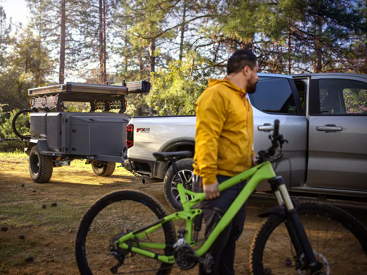 A 2025 Ford Ranger® with trailer hooked up and a man holding his bike in foreground