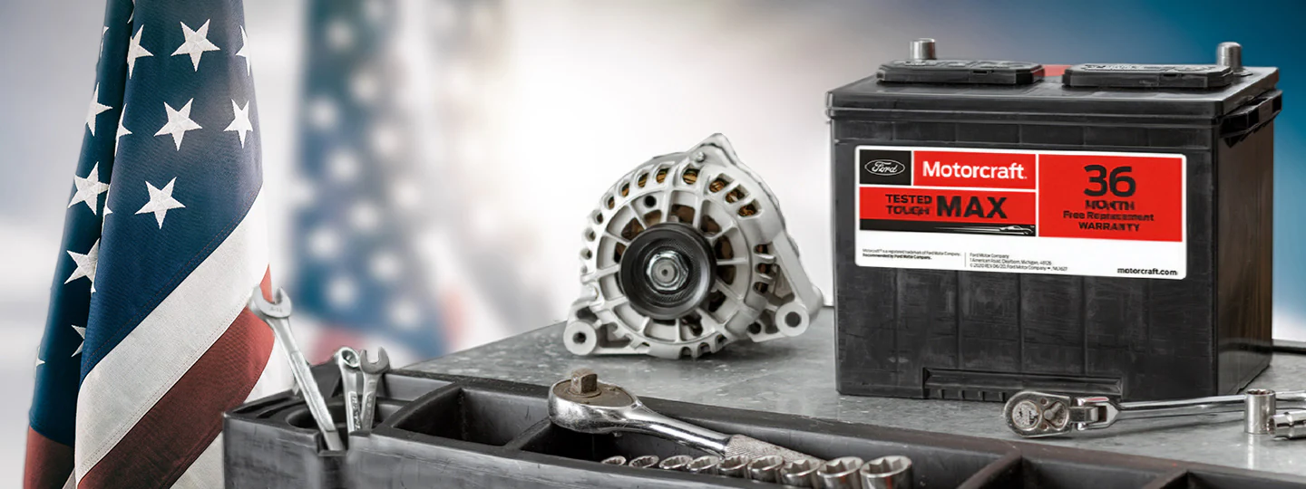 Ford Motorcraft® car battery and alternator on a workbench with automotive tools, American flag in background