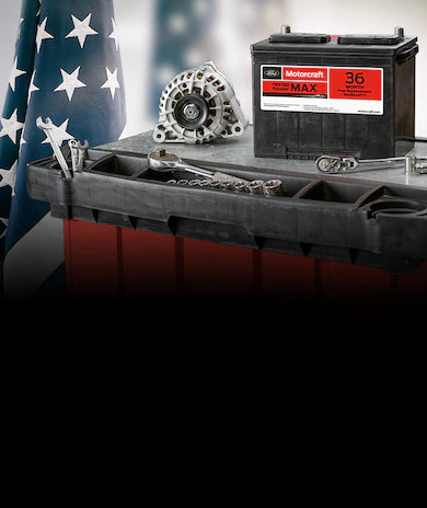 Ford Motorcraft® car battery and alternator on a workbench with automotive tools, American flag in background